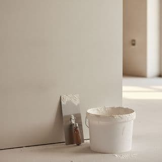 A smoothly plastered wall with a bucket of plaster and tools on the floor in front of it.